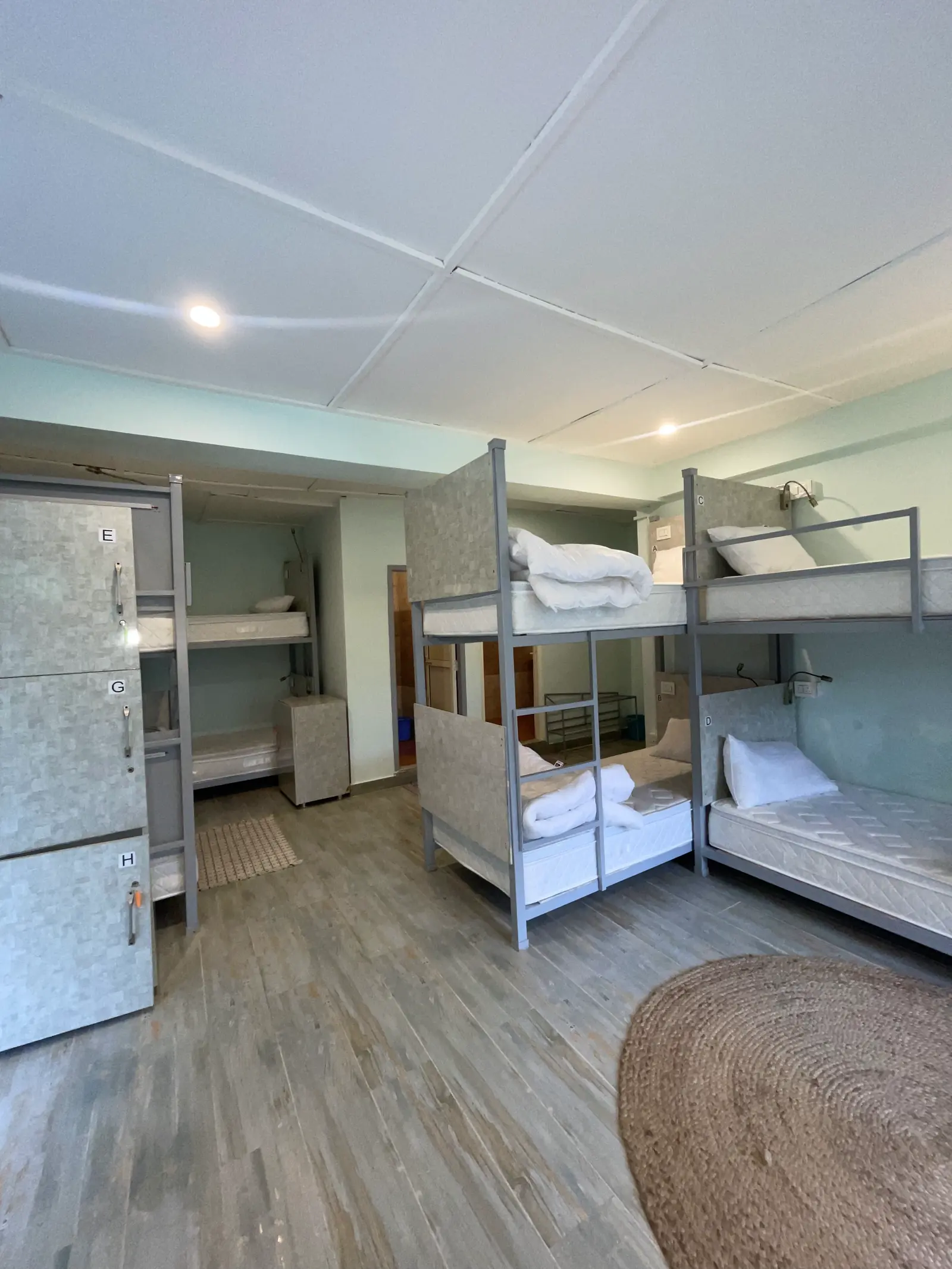 The eight-bed mixed dorm, lettered lockers along one wall and bunks along the other