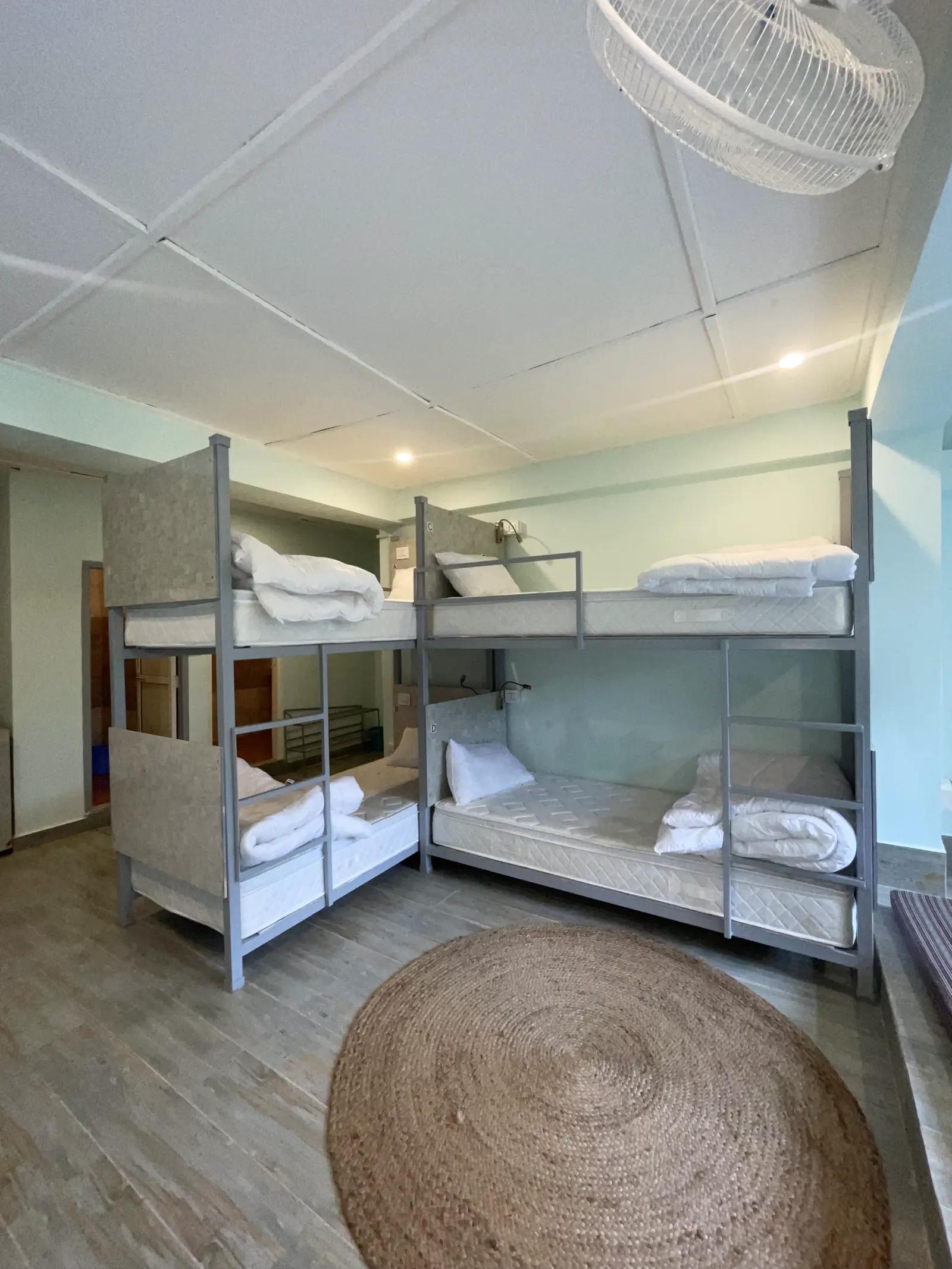 Two metal bunk units at right angles in the eight-bed dorm, with a round jute rug