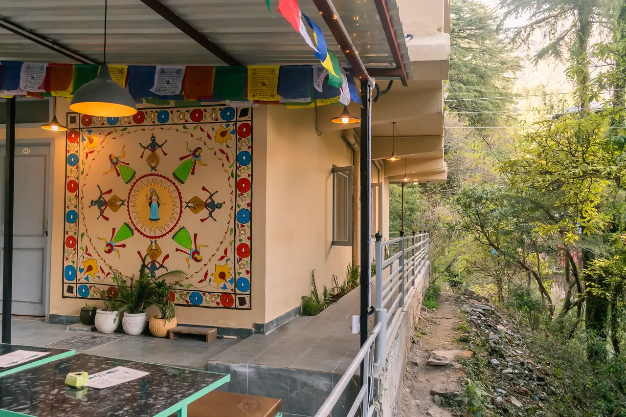 The covered walkway with its painted mandala mural, potted plants and prayer flags
