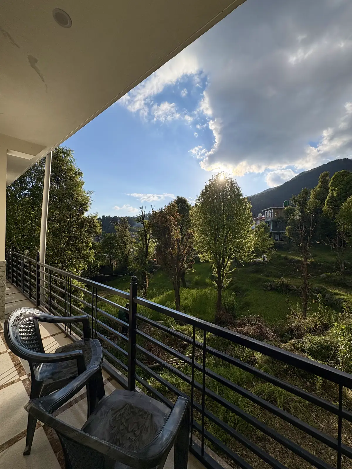 A balcony with two chairs and a metal railing, looking onto trees and a grassy slope