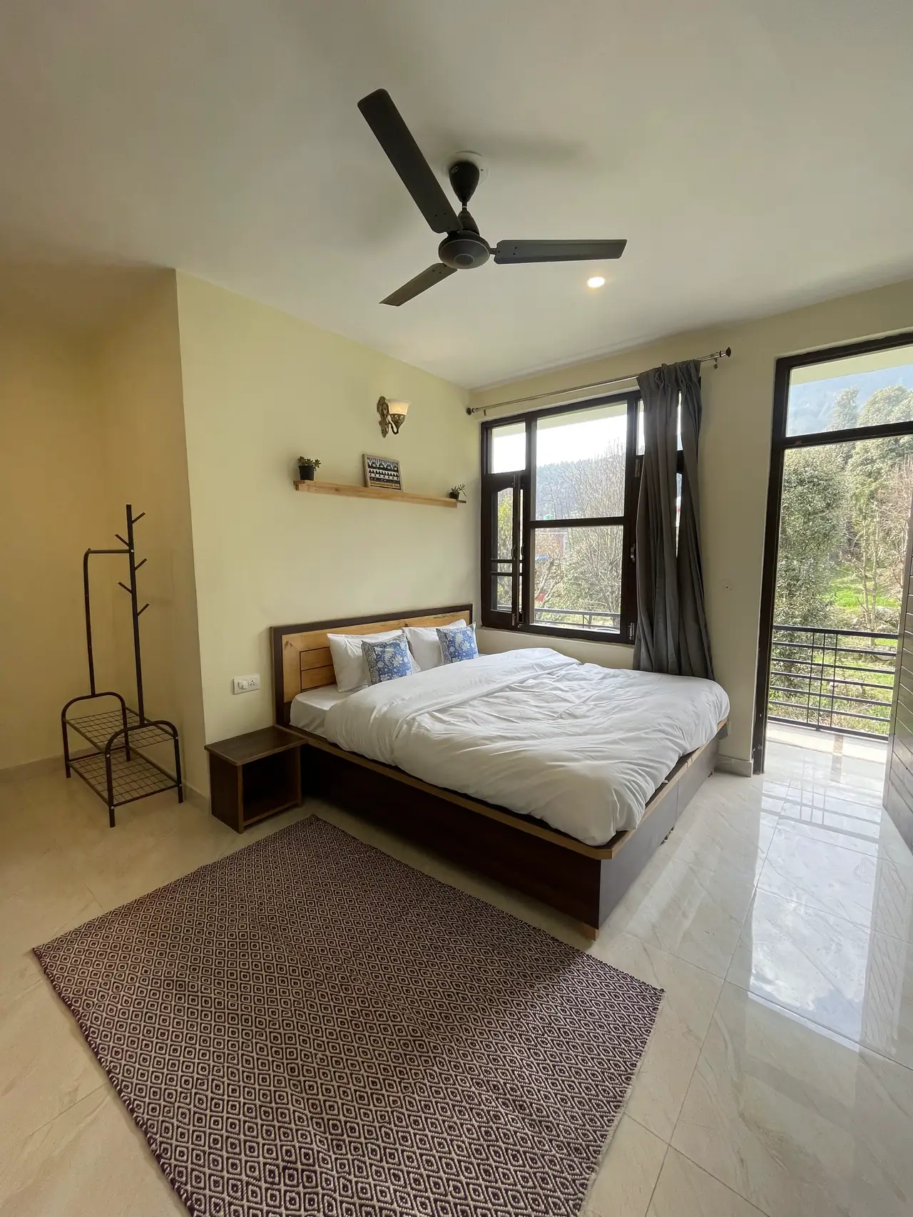 A king room with a coat rack and rug, an open door onto the railed balcony