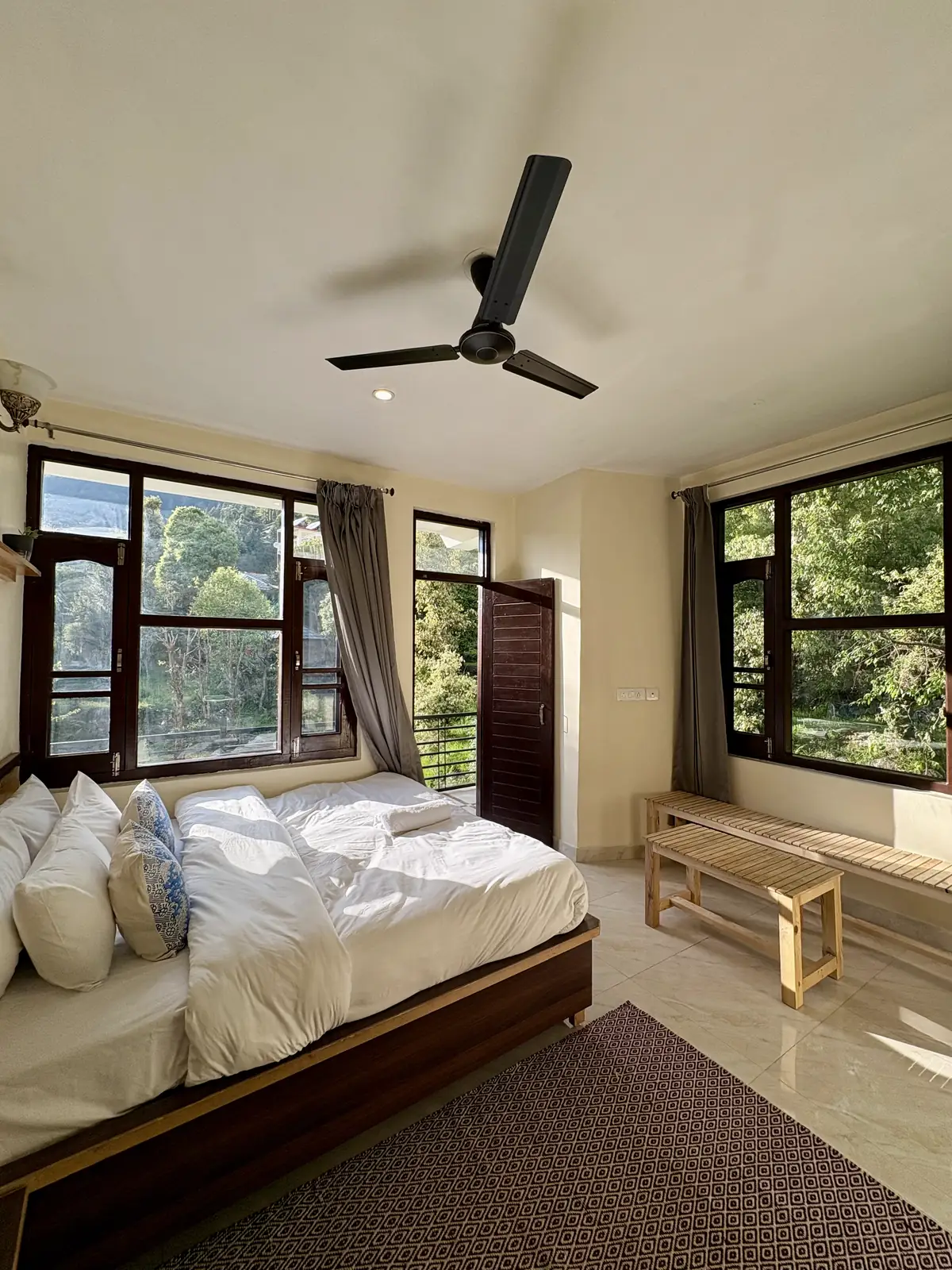 A king room in daylight, the bed between two windows full of green and a slatted bench