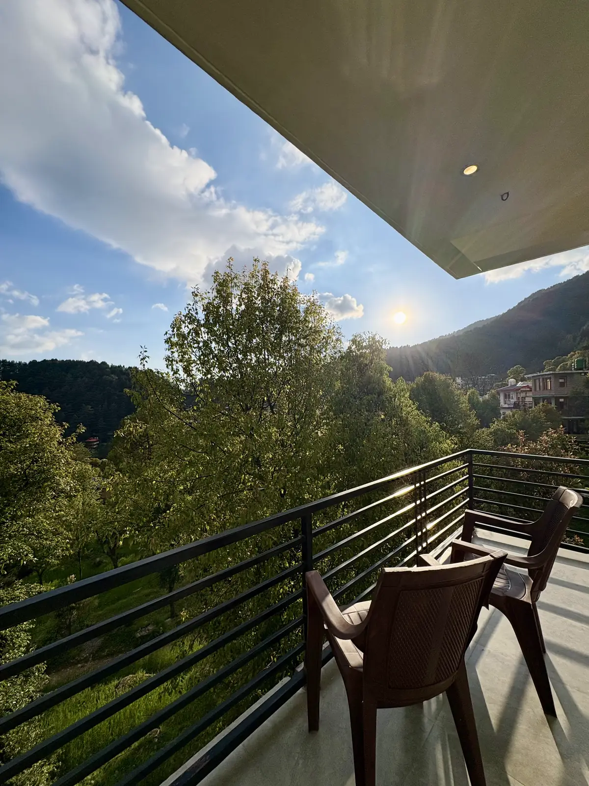 The studio balcony in low sun, two chairs above a forested ridge and terraced slope