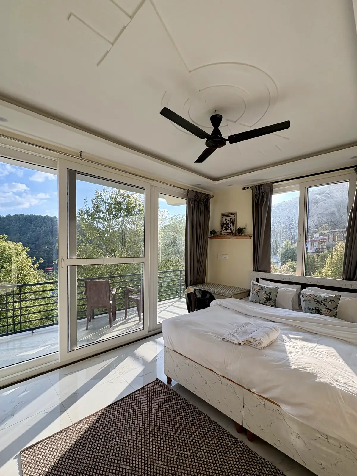 A sunlit studio with a wide bed, ceiling fan and full-height glazing onto the balcony