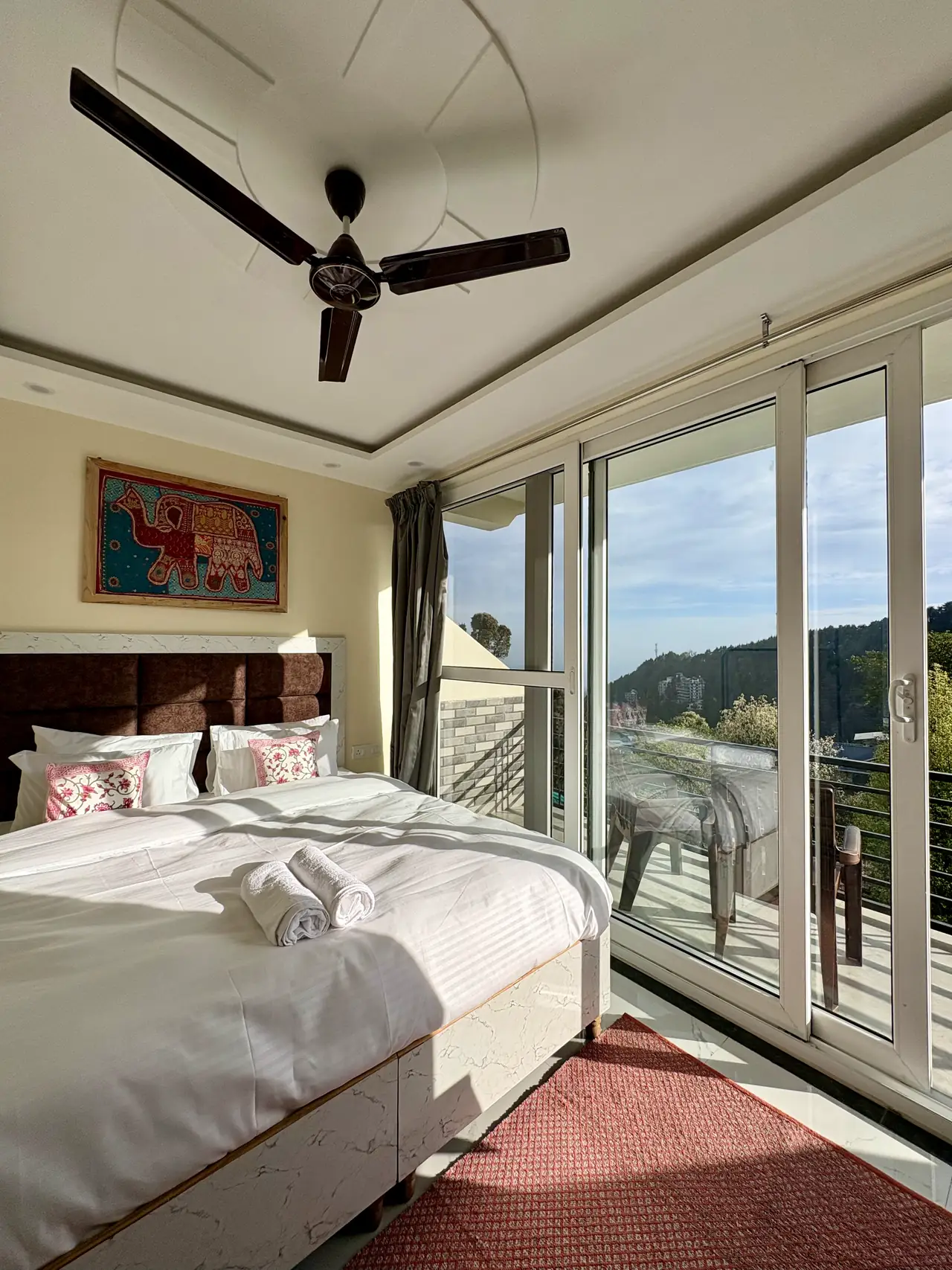 A superior king room with a framed elephant textile, red rug and doors onto the balcony