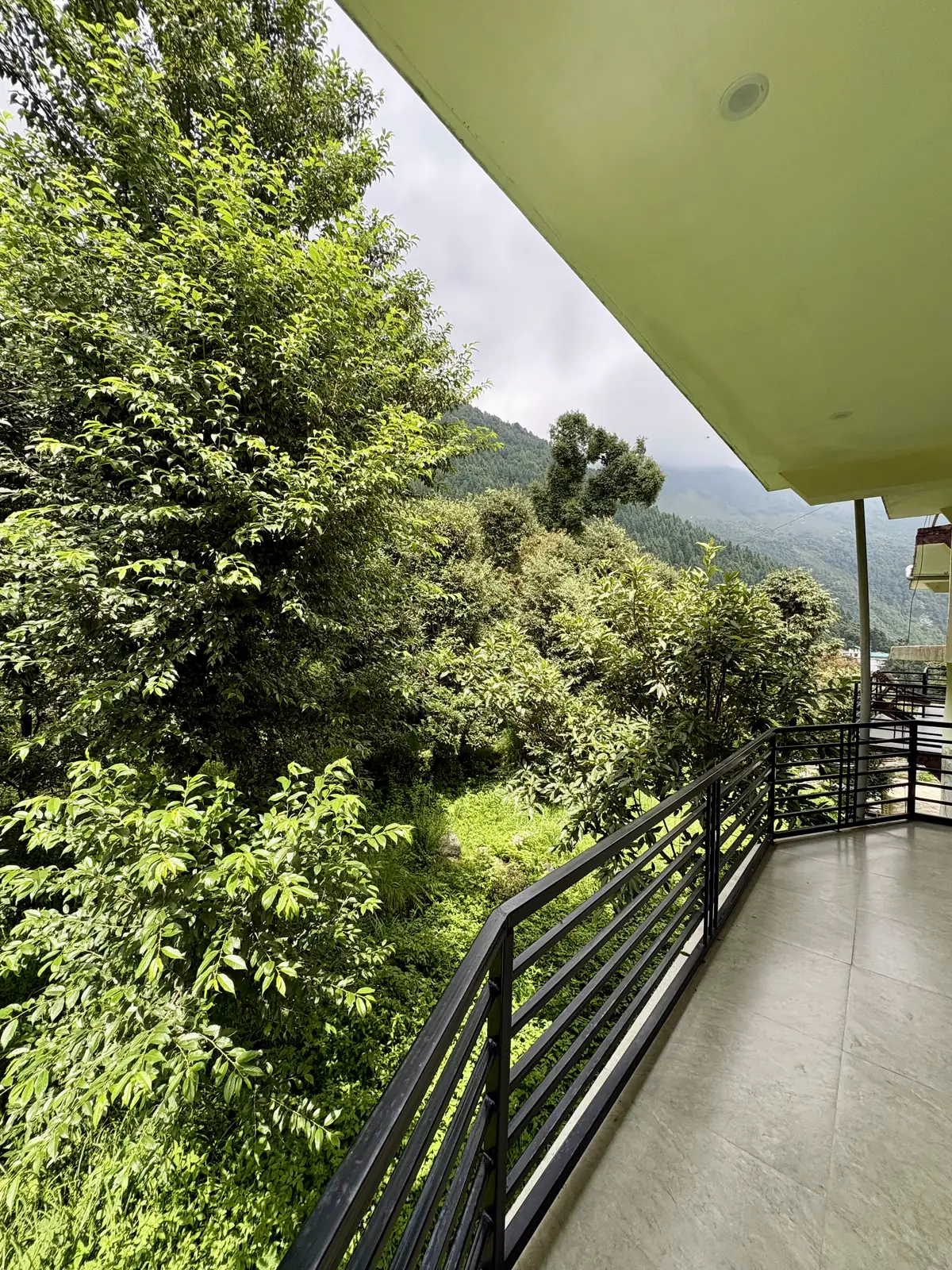 The tiled balcony running along its railing, dense green trees and a distant ridge